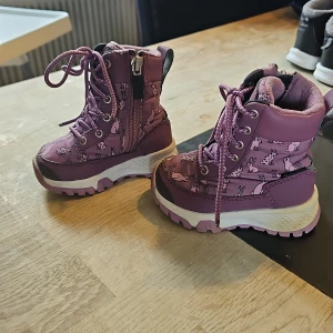 Lavendelfärgade Gulliver kängor EU20 - Säljer ett par gulliga lavendelfärgade kängor från Gulliver med Gore-Tex. Skorna har snörning, dragkedja på sidan och ett mönster med söta kaniner. Grov platt sula och fleecefoder gör dem perfekta för kalla dagar. Modell: Lungan Gesunda GTX. Finns tecken på lek i sandlåda men mest använda i vagn. Snörena är avklippta och brända för att inte teådas upp, dom va jättelånga så är därför.