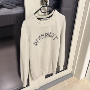 Vit sweatshirt från Givenchy - Vit sweatshirt från Givenchy med broderad logga i svart på bröstet. Tröjan har rund hals, ribbade muddar och lång ärm. Materialet är mjuk bomull som känns skönt mot huden. Perfekt för dig som gillar stilrena designer och exklusiva märken.