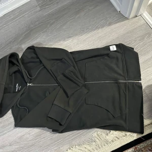 Svart hoodie med dragkedja Jack & Jones - Svart hoodie från Jack & Jones Essentials i storlek S. Tröjan har hel dragkedja framtill, två stora fickor och huva med snörning. Tillverkad i mjuk bomullsmix, perfekt för chill dagar eller när du vill ha en enkel och stilren look.