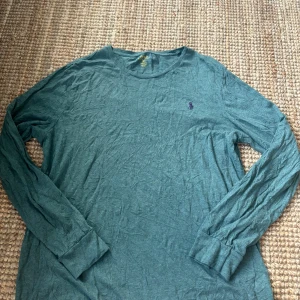 Grå långärmad tröja från Polo Ralph Lauren - Snygg grå långärmad tröja från Polo Ralph Lauren i 100% bomull. Tröjan har en klassisk passform och är dekorerad med det ikoniska lila broderade logotypen på bröstet. Perfekt för en chill och stilren look. Skriv ifall ni har fler frågor eller vill se fler bilder och kolla gärna in min profil ❣️❣️