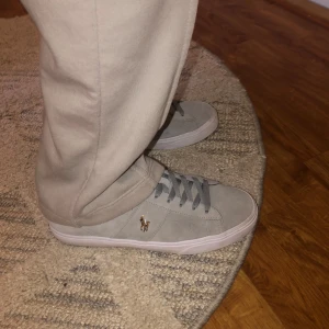 Grå mockasneakers från Polo Ralph Lauren - Snygga grå sneakers från Polo Ralph Lauren i mocka med klassisk låg profil och vit sula. Skorna har grå snörning och den ikoniska Polo-loggan i guld på sidan. Perfekta för en clean och stilren look. Skorna är bara använda 4-5 gånger.