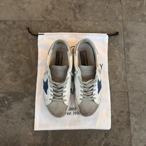 Golden Goose Superstar - Golden Goose Superstar sneakers i vitt skinn med grå mockadetaljer och silverfärgad häl. Sällsynt modell som inte syns alltför ofta. Flitigt använda men defekterna kan fixas hos skomakare vid behov. Box dustbag tillkommer självklart. Hör av dig vid minsta fundering! Pris kan diskuteras