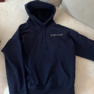 Marinblå hoodie från Polo Ralph Lauren - Säljer en marinblå hoodie från Polo Ralph Lauren med broderad logga på bröstet. Tröjan har huva med snörning och en stor magficka. Perfekt för dig som gillar klassisk och stilren hoodie. S men sitter mer åt de baggy hållet som en skön hoddie ska.