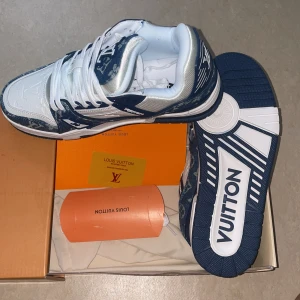 Louis Vuitton blå/vita sneakers - Säljer ett par Louis Vuitton sneakers i blått och vitt med klassiskt monogrammönster. Skorna har snörning, rund tå och platt sula. Ovandelen är i denim och skinn med tydliga LV-detaljer på tunga och häl. Perfekta för dig som vill sticka ut med lyxig streetstyle. Storlek 41 och passar 40, priset kan diskuteras 
