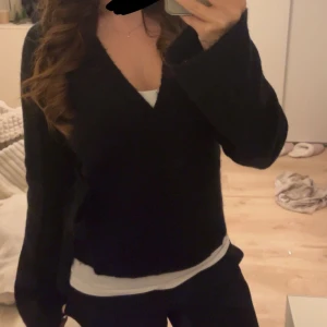 Svart omlottkofta med v-ringning - Mysig svart omlottkofta med djup v-ringning och långa ärmar. Koftan är perfekt att ha över ett linne. Från Gina i storlek M men är som en S ⭐️