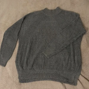 Grå stickad tröja från H&M Divided - Mysig grå stickad tröja från H&M Divided med ribbad struktur och högre krage. Perfekt för lager-på-lager under kyliga dagar. Långärmad och i klassisk modell som funkar till allt.