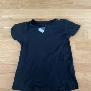 Svart basic t-shirt från 157 - En svart basic t-shirt från 157 med rund hals och korta ärmar. Tillverkad i mjuk bomullsmix (94% bomull, 6% elastan) som ger en skön och stretchig passform. Perfekt till jeans eller shorts för en enkel och clean look.