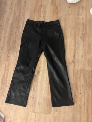 Svarta skinnbyxor från Bik Bok - Snygga svarta skinnbyxor från Bik Bok i rak modell med normal passform och låg/mellan hög midja. Byxorna har klassiska fickor bak och stängs med knapp och dragkedja. 