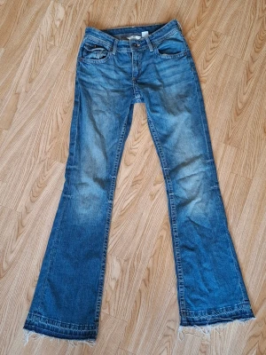 Blå bootcut jeans från H&M, stl 164 - Snygga blå jeans från H&M med bootcut och låg midja. Jeansen har justerbar midja, klassiska fem fickor och cool broderad detalj på bakfickorna. 💕
