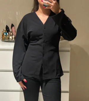Svart v-ringad skjorta från H&M - Säljer denna helt oanvända svarta figurnära skjortan med knappar och v-ring. Skjortan är från H&M och i storlek S!