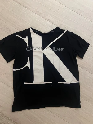 Svart t-shirt från Calvin Klein Jeans - Säljer en svart t-shirt från Calvin Klein Jeans med stor vit CK-logga över hela framsidan och tryckt text