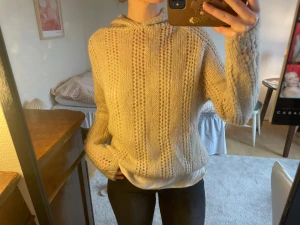 Beige stickad hoodie med huva - Mysig beige stickad hoodie med huva och lång ärm. Tröjan har ett snyggt hålmönster i lodräta ränder och en relaxed passform. Perfekt för lager-på-lager och chill dagar. Passar dig som gillar en enkel men ändå trendig look.