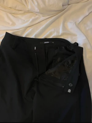 Svarta kostymbyxor från Bik Bok - Snygga svarta kostymbyxor från Bik Bok i klassisk rak modell med dragkedja och knappstängning. Byxorna har en stilren look och är tillverkade i ett mjukt tyg som ger en skön passform. Perfekta för dig som gillar minimalistisk stil.