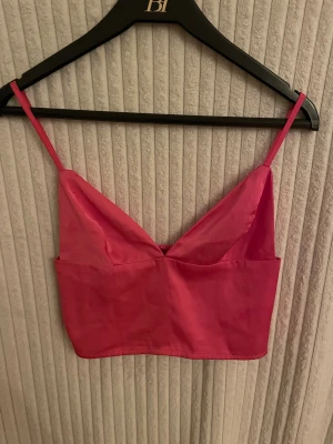 Rosa satin linnetopp med smala band - Snygg rosa linnetopp i satin med smala axelband och v-ringad front. Toppen är croppad. I bra skick och säljs i befintligt skick. 
