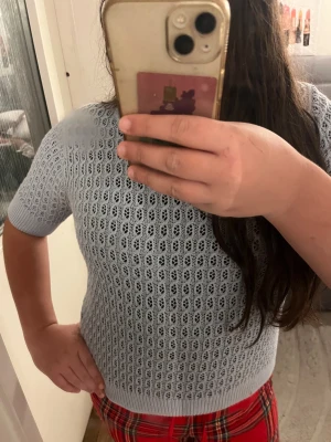 Ljusblå stickad tröja från 157 XS - Supersöt ljusblå stickad tröja från 157 i storlek XS. Tröjan har ett snyggt hålmönster och ribbade kanter vid hals, ärmslut och nederkant. Kortärmad och perfekt för vår och sommar. Enkel att styla med jeans eller kjol för en chill look.