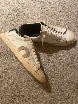 Oliver Cabell Sneakers - Säljer ett par vita sneakers med svart häl, skorna har snörning, platt sula och rund tå. Tillverkade i skinn och mocka, med klassisk låg profil och stilren look. Använda i cirka 3 månader. Dm för frågor!