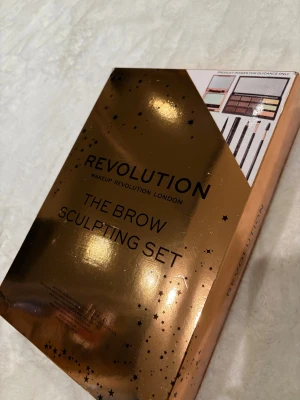 Revolution Brow Sculpting Set - Perfekt för julklappar ! Snyggt brow sculpting set från Revolution med metallic guldig förpackning. Innehåller brynpalett med flera nyanser, brynpennor, borstar och spoolie för att forma och fylla i brynen. Perfekt för att skapa definierade och naturliga bryn. Allt du behöver för din brow-rutin. Förpackningen är helt ny aldrig använd 