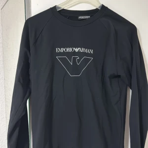 Svart långärmad tröja Emporio Armani - Svart långärmad tröja från Emporio Armani med stort vitt logotryck på bröstet. Tröjan har rund hals och är tillverkad i mjukt material som känns skönt mot huden. Storlek S men passar M 