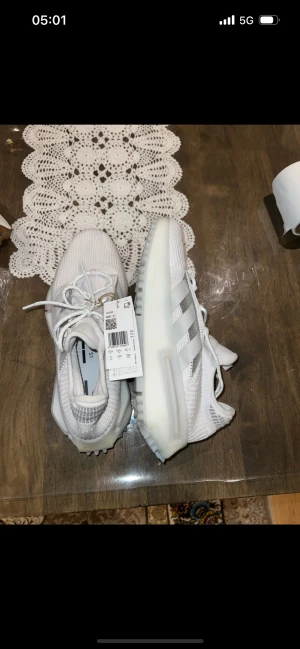 Adidas NMD S1 vita sneakers - Säljer ett par Adidas NMD S1 sneakers i helvitt med klassiska tre ränder på sidan. Skorna har en chunky sula med grovt mönster, stickad ovandel i syntet och snörning. Perfekta för dig som gillar modern och sportig stil.