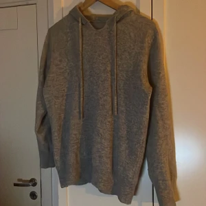 Grå merino hoodie - Säljer en stilren grå hoodie med dragsko i huvan. Perfekt för en avslappnad look. Tröjan har långa ärmar och en mjuk känsla. Passar bra till både jeans och joggers.
