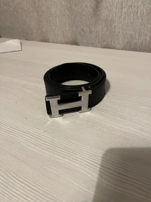 Svart H-bälte - Säljer ett svart bälte på 130 cm. Det är ganska slitet men det syns inte så tydligt.