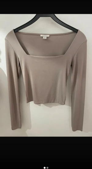 Beige långärmad topp från Amisu - Säljer en stilren beige långärmad topp från Amisu med fyrkantig halsringning och croppad passform. Mjuk och stretchig i materialet, perfekt för att skapa en clean och trendig look. Enkel att matcha med både jeans och kjol.
