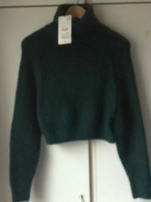 Mörkgrön croppad polotröja - Snygg mörkgrön croppad polotröja med lång ärm och hög krage. Stickad i mjukt material som ger en skön känsla och passar perfekt till höst och vinter. Enkel design utan mönster, perfekt att matcha med jeans eller kjol.