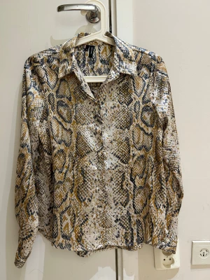  Ny Ormskinnsmönstrad skjorta från Zara  - Säljer en skjorta från Zara  med ormskinnsmönster i beige, grått och brunt. Skjortan har klassisk krage, knappar framtill och långa ärmar. Materialet är lätt och känns skönt mot huden, perfekt för dig som gillar att sticka ut med coola prints.