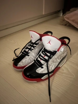 Nike Jordan sneakers svart/vit/röd - Säljer ett par Nike Jordan sneakers med högt skaft. Skorna har svart lackad tå, vit ovandel med grafiskt mönster och röda detaljer. Tungan är vit med röd Jumpman-logga och insidan är röd. Svart snörning och platt sula i rött, vitt och grått. Perfekt för dig som gillar streetstyle.