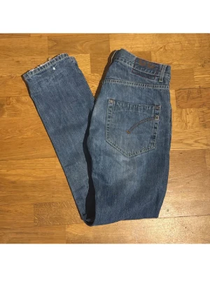 Blå jeansbyxor i rak modell, storlek 32 - Säljer ett par klassiska blå jeansbyxor i rak passform med fem fickor och knappgylf. Jeansen har snygga slitningar och kontrastsömmar, tillverkade i 100% bomull. Perfekta för dig som gillar en tidlös och avslappnad stil.