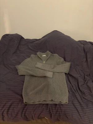 Grå ribbad stickad tröja med half zip - Säljer en grå stickad tröja från  med ribbad struktur och half zip framtill. Tröjan har lång ärm och en hög krage som ger en chill och snygg look. Perfekt för dig som gillar enkel och stilren design.