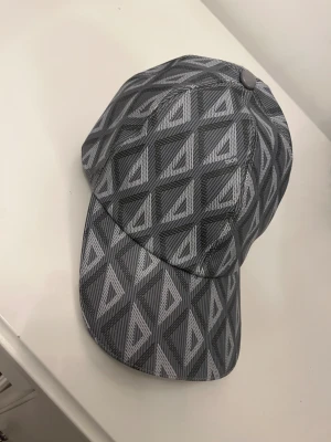 Dior keps - Snygg keps från Dior i grått med geometriskt mönster. Använd väldigt få gånger och är som ny! Storlek L men går att justera själv.