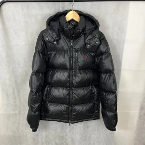 Polo Ralph Lauren Glossy Jacka - Snygg svart dunjacka från Polo Ralph Lauren med röd logga på bröstet. Nyskick, kvitto finns, QR kod finns, inga defekter. 