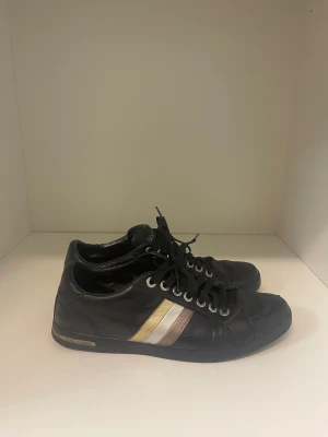 Svarta  Dolce & Gabbana skor - Svarta sneakers från Dolce & Gabbana i skinn med snörning och platt sula. Sidan har två stilrena ränder i guld och silver som ger en lyxig touch. Rund tå och metallfärgade öljetter för snören. Perfekt för dig som gillar klassisk design med exklusiv känsla.