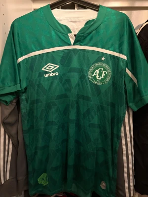 Grön Chapecoense fotbollströja Umbro - Full autentisk Chapecoense matchtröja från Umbro i grön färg med geometriskt mönster och vita detaljer. 