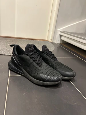 Nike Air Max 270 svarta sneakers - Svarta Nike Air Max 270 sneakers med mesh-överdel och synlig Air-enhet i hälen. Snygg sportig look med snörning och platt sula. Perfekt för dig som gillar streetstyle och vill ha bekväma skor med modern design.