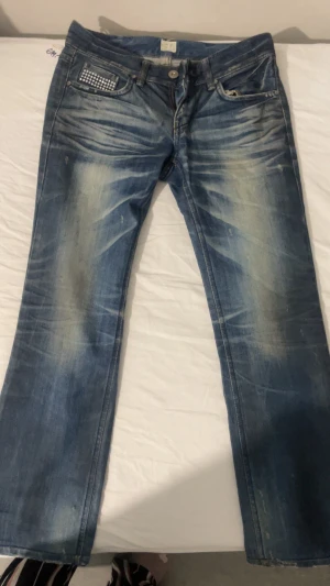 Lowwaist Yeomigo Jeans 90s - Snygga blå jeans från Yeomigo Jeans med coola slitningar och ljusa tvättade detaljer. Fickorna är dekorerade med silvriga nitar som ger extra edge.  Väldigt lågmidjade som från 90s och är bootcut (: