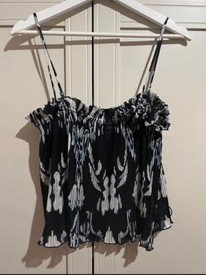 Topp h&m - Säljer en flowy linnetopp i svart och vitt med blommigt mönster och tunna axelband. Stretchig vid bysten så passar allt från xs-m