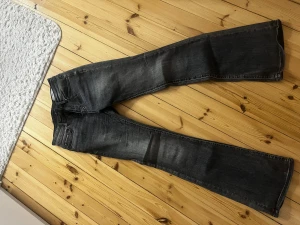 Bootcut jeans i mörkgrå denim - Snygga bootcut jeans i mörkgrå tvättad denim med klassisk femficksdesign och bälteshällor. Jeansen har en rak passform över låren och blir vidare nedtill, vilket ger en cool siluett. Perfekta att matcha med sneakers eller boots för en avslappnad look.