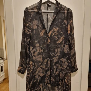Svart långskjorta/kaftan  - Snygg kaftan i transparent svart tyg med stora romantiska rosor. Finns ej att köpa längre. Snygg dekoration till vilken enkel outfit som helst. Storlek XS men passar mig som har S också.