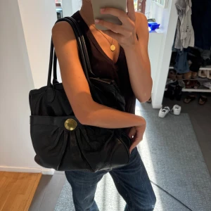 Svart skinnväska Marc by Marc Jacobs - Säljer en svart handväska i skinn från Marc by Marc Jacobs med snyggt veckad framsida och guldigt logomärke. Väskan har långa handtag och ett färgglatt mönstrat innerfoder. Perfekt för dig som vill ha plats med allt du behöver till båda skola eller en vanlig jobbdag. Vintage och unikt mönster inuti som jag älskar. Väskan har en mindre skada på själva dragkedjan men jag har alltid kunnat stänga min väska ändå men därför ja sänkt lite på priset!! Unik och tidlös då den funkar till ALLT 💗💗