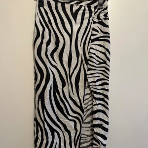Zebramönstrad långkjol i linne - Snygg långkjol från H&M med zebramönster i svart och vitt. Kjolen har rak passform och är tillverkad i ett lätt linnematerial som känns luftigt. Perfekt för dig som vill sticka ut med ett djurmönster och gillar trendiga detaljer.