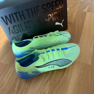 Puma fotbollsskor gul/blå - Snygga fotbollsskor från Puma i neon-gult och blått med svarta detaljer och svensk flagga på sidan. Dem är helt oanvända storlek 41.