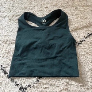 Mörkgrön sporttopp från lager 157 X-Small - Sportig mörkgrön linnetopp från lager 157 i storlek X-Small. Toppen har brottarrygg och bred ribbad kant nedtill för extra stöd. Perfekt för träning och aktiva dagar. Snygg och enkel design som är lätt att matcha med andra träningskläder.
