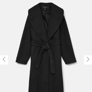 Svart lång kappa - Snygg svart kappa från Vero Moda med bred krage och knytbälte i midjan. Långärmad och med klassisk rak passform, perfekt för dig som vill ha en stilren look. Materialet är mjukt och känns lyxigt, och kappan har en tidlös design.