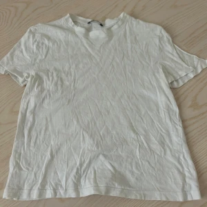 Vit basic t-shirt i bomull - En enkel vit t-shirt med rund hals och korta ärmar. Tillverkad i mjuk bomull, perfekt för en clean och avslappnad stil. Passformen är normal och t-shirten är helt utan mönster eller detaljer. Ett måste i garderoben för dig som gillar minimalistiskt.