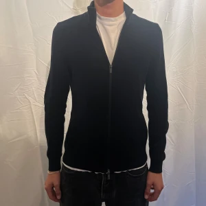  Ziptröja från Massimo Dutti - Stilren marinblå tröja från Massimo Dutti med hel dragkedja framtill. Modellen har hög krage och lång ärm, perfekt för lager-på-lager och kyliga höst dagar. Passformen är normal och materialet känns mjukt och bekvämt mot huden. Modellen är 180cm
