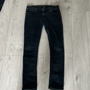 Mörkblå jeans från Nudie Jeans, W31 L32 - Snygga svarta jeans från Nudie Jeans med klassisk femficksdesign och smal passform. Jeansen har mörk tvätt och subtila slitningar, tillverkade i mjukt denimtyg som sitter skönt hela dagen. Perfekta för dig som gillar stilrena och tidlösa jeans.