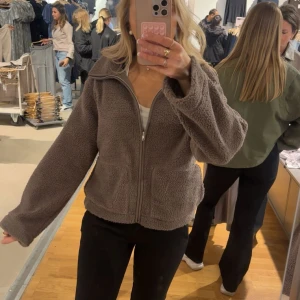 Brun teddyjacka med dragkedja - Mysig brun teddyjacka med breda ärmar och två stora fickor framtill. Jackan har en hel dragkedja och är perfekt för att hålla sig varm och se chill ut. Fleece-liknande material som känns mjukt och skönt mot huden.