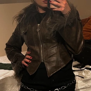 Brun skinnjacka med fuskpäls från Aelfric Eden - Säljer en brun skinnjacka från Alfric Eden med fluffig fuskpäls vid krage och ärmslut. Jackan har en snygg croppad passform, markerad midja, två bröstfickor med knappar och dragkedja framtill med hjärtformad zip. Vadderad med flis så den passar perfekt till hösten🍂 Köpte en förstor och beställde rätt storlek, har därför två hemma. Bilderna på mig är från min jacka och inte på den jag säljer. Den är helt oanvänd 